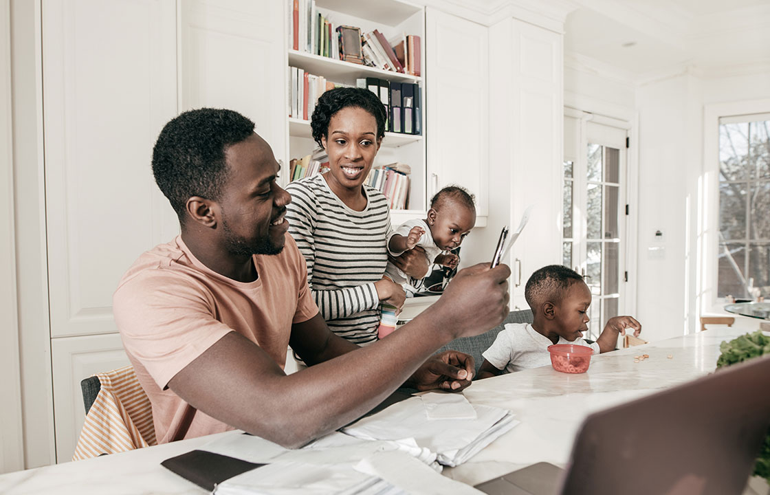 man holding document while wife who is holding a paper looks on and younger child eats nearby